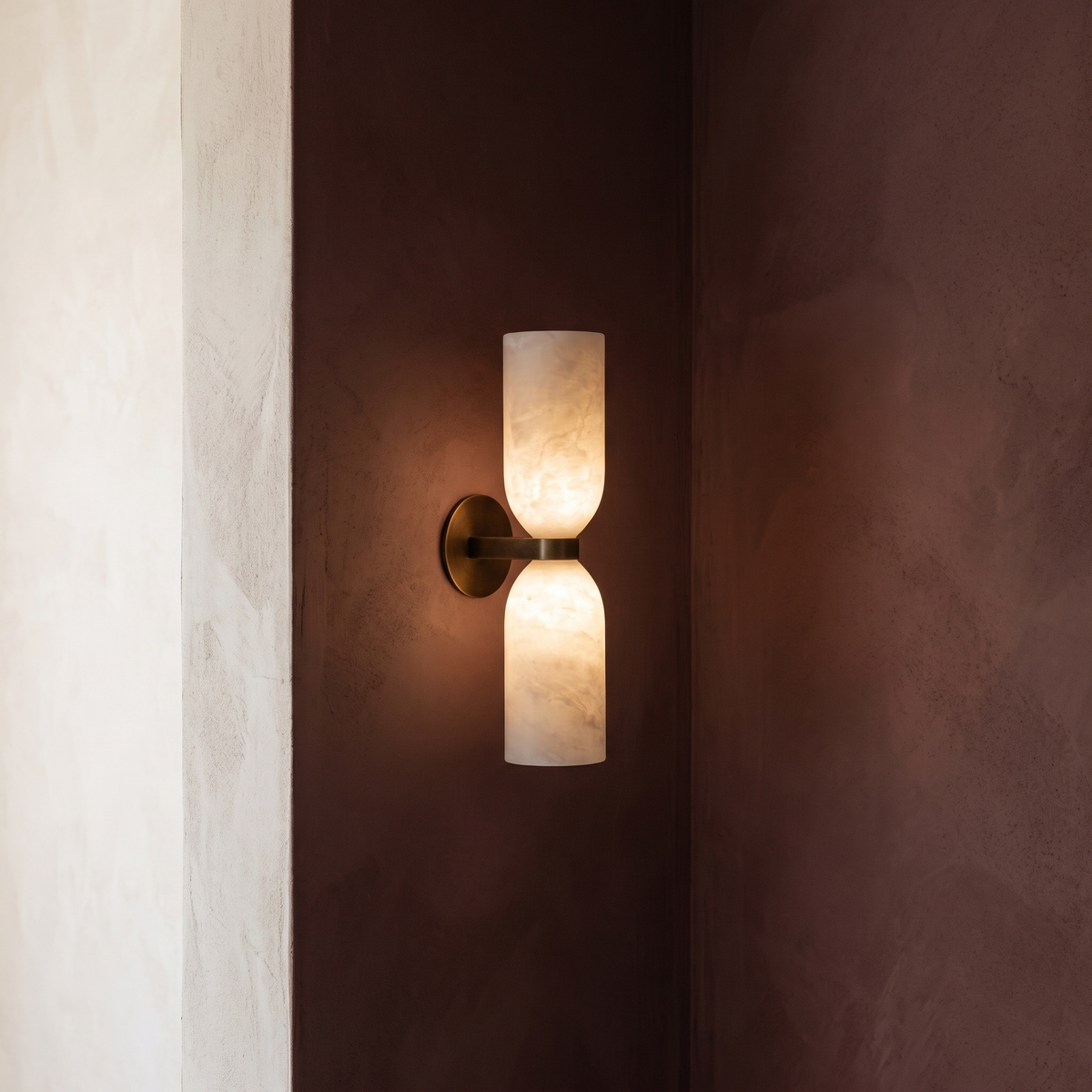 Alabaster double wall sconce glowing warm on a plaster wall