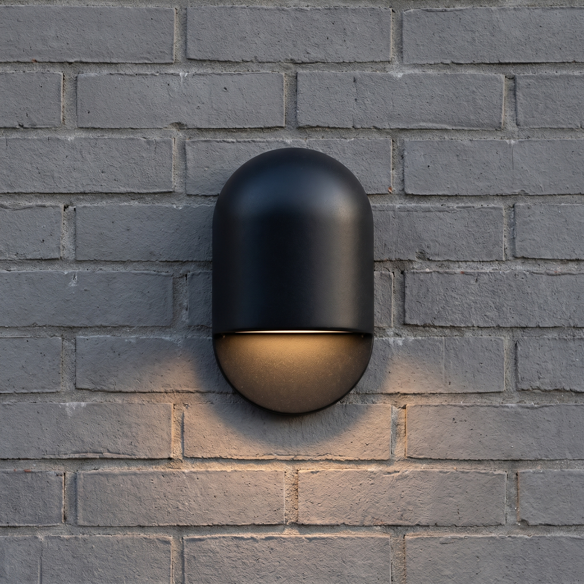 AX472 black outdoor wall light casting a warm downlight wash across a grey brick wall